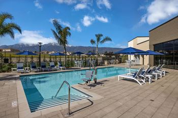 A swimming pool with chairs and umbrellas and mountains in the background