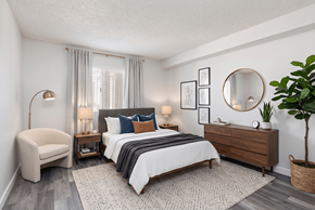 Phoenix apartment for rent - A bedroom with a large bed, a chair, a side table with lamps, a dresser, and a potted plant.