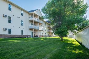 Fargo apartment for rent - a large grassy area with a tree in front of an apartment building at Bluemont Village Apartments, Fargo