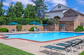 Phoenixville apartment for rent - Swimming pool surrounded by lounge chairs and tables and adorned with tall trees.