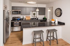 Phoenixville apartment for rent - Kitchen with dark cabinets, quartz counters, and a peninsula with two chairs behind it.