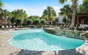 Conroe apartment for rent - A swimming pool surrounded by palm trees and lounge chairs.