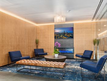 A lobby with blue chairs and a table and a painting on the wall