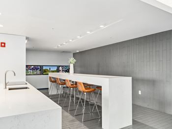 A kitchen with white marble countertops and a bar with orange chairs