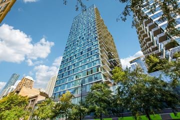 Chicago apartment for rent - A tall building with many windows stands in front of other buildings and trees.