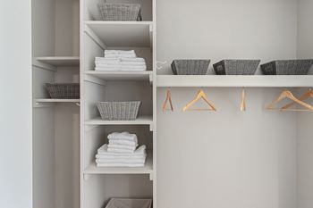 A white shelving unit with baskets and hangers and folded white towels