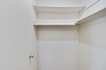 A walk in closet in a bedroom with white walls and a white ceiling with a skyl