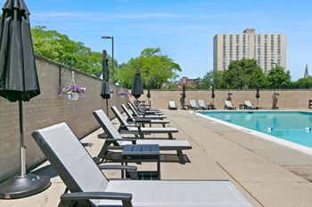 A row of sun loungers are on the patio of a pool
