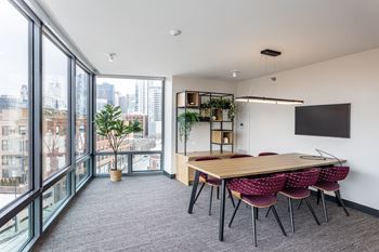 A conference room with a long table and chairs, a tv on the wall, and a view of the city outside the windows.