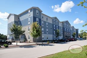 Knoxville apartment for rent - The front of a large blue and grey apartment building surrounded by lush green trees.