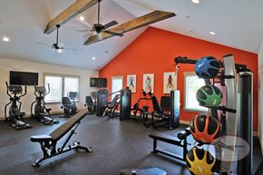 Johnson City townhouse for rent - A fitness center with an orange accent wall, large windows, flat screen TVs, with weight training and cardio equipment.