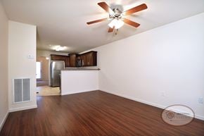 Gray townhouse for rent - The living room with vinyl hardwood flooring, white walls, and a ceiling fan with a bar and kitchen in the background..