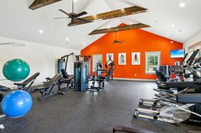 Powell townhouse for rent - A fitness center with an orange accent wall, exposed beams, and weight lifting and cardio equipment.