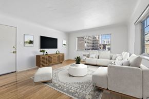 Denver apartment for rent - A living room with a white couch, a white chair, a wooden cabinet, and a flat screen TV.