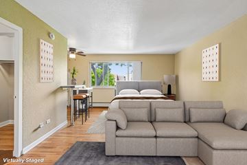 Denver apartment for rent - A living room with a grey couch and a bed in the background.