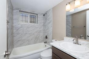Denver apartment for rent - A white bathtub sits next to a toilet in a bathroom with marble tiles.