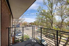 Denver apartment for rent - A balcony with a black railing overlooks a parking lot and trees.