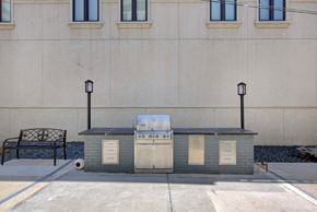 Denver apartment for rent - A small grey building with a white door and windows is situated in front of a building with windows.