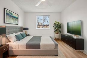 Denver apartment for rent - A bedroom with a large bed, a television, and a window with a view of a building outside.