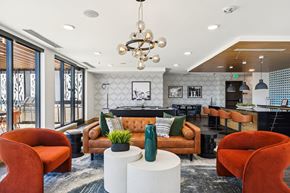 Denver apartment for rent - A modern living room with a brown sofa, orange chairs, and a chandelier.