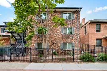 Denver apartment for rent - A brick building with a black fence and a tree in front.