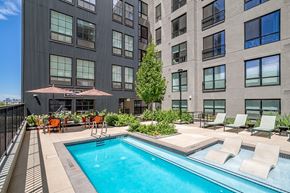Denver apartment for rent - A pool surrounded by chairs and umbrellas in front of a building.