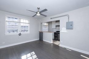 Denver apartment for rent - A room with a ceiling fan and a kitchen area in the background.