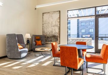 Elkhorn apartment for rent - A modern living room with a grey chair, orange chairs, and a large abstract painting on the wall.
