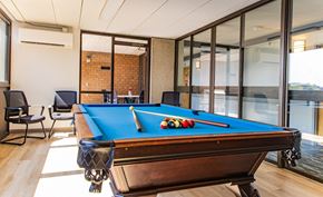 Medford apartment for rent - Billiards room with a pool table with a green cloth and white cue balls is in the foreground of a room with a brick wall and sliding glass doors.