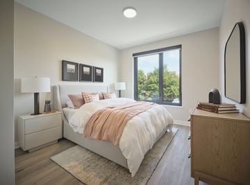 Chicago apartment for rent - A bedroom with a large bed, a nightstand with a lamp, a dresser, and a window with a view of trees.