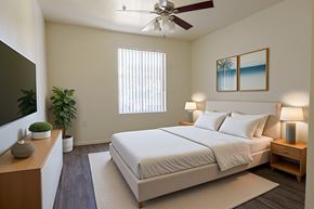 Las Vegas apartment for rent - A bedroom with a large bed, a ceiling fan, and a painting of a beach scene on the wall.