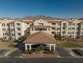 Las Vegas apartment for rent - A large building with a brown roof is surrounded by other buildings and palm trees.