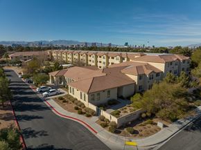 Las Vegas apartment for rent - A large building with a red roof is surrounded by a parking lot and trees.