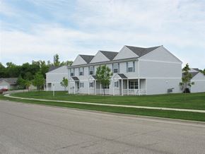 Sioux Falls townhouse for rent - A white house with a grey roof is surrounded by a green lawn.