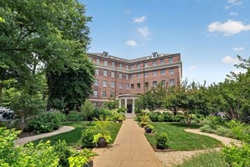 Washington apartment for rent - A large building with a red brick exterior is surrounded by a well-manicured garden with a gravel path leading to the entrance.
