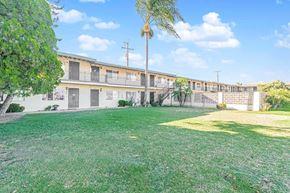 Downey multi-family for rent - A grassy area in front of a building with a tree and bushes.
