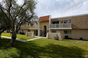 Hemet multi-family for rent - A building with a red roof and a tree in front of it.
