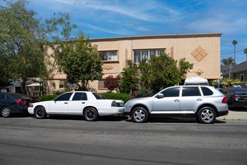 Los Angeles multi-family for rent - Two cars parked in front of a tan building with trees in the background.