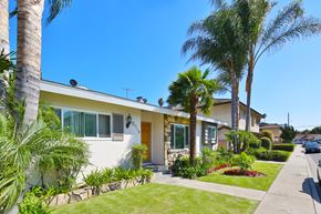 Downey multi-family for rent - A house with a white exterior and a brown door is surrounded by palm trees.