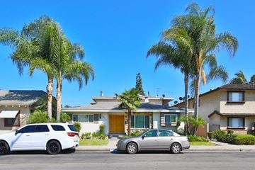 Downey multi-family for rent - Two cars are parked in front of a house with palm trees.