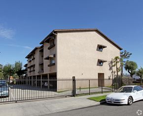 South Gate multi-family for rent - A white car is parked in front of a beige building with a black fence.