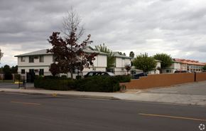 Perris multi-family for rent - A white building with a green roof is surrounded by a black fence.