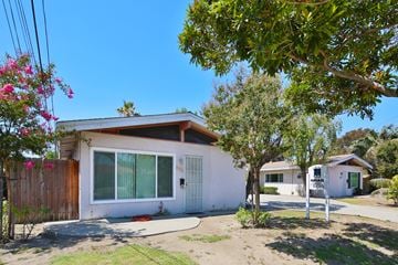 Downey multi-family for rent - A house with a white exterior and a brown roof is surrounded by greenery and a clear blue sky.