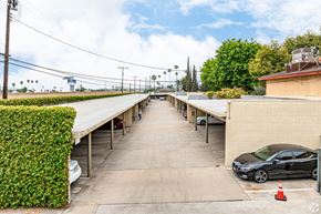 Claremont multi-family for rent - A black car is parked in a parking lot with a green hedge on the left.
