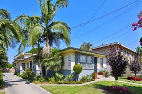 Downey apartment for rent - A house with a blue and yellow facade is surrounded by greenery and a clear blue sky.