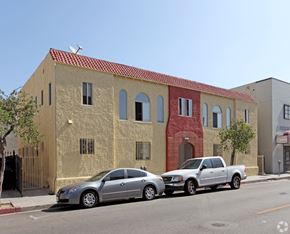 Huntington Park multi-family for rent - Two cars parked in front of a tan building with a red tile roof.