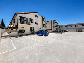 Gardena multi-family for rent - A blue car is parked in a parking lot in front of a building with the number 1214 on it.
