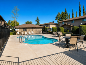 Merced multi-family for rent - A pool surrounded by chairs and a table with a house in the background.