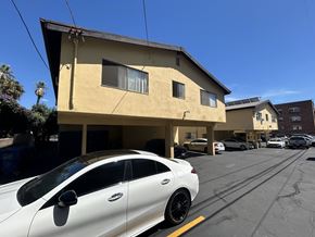 Los Angeles apartment for rent - A white car is parked in a parking lot in front of a yellow building.