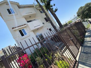 Los Angeles multi-family for rent - A tall white building with a brown gate and plants in front.